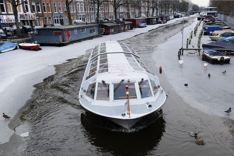 Een rondvaartboot baant zich een weg door de bevroren grachten in  Amsterdam. Beeld 