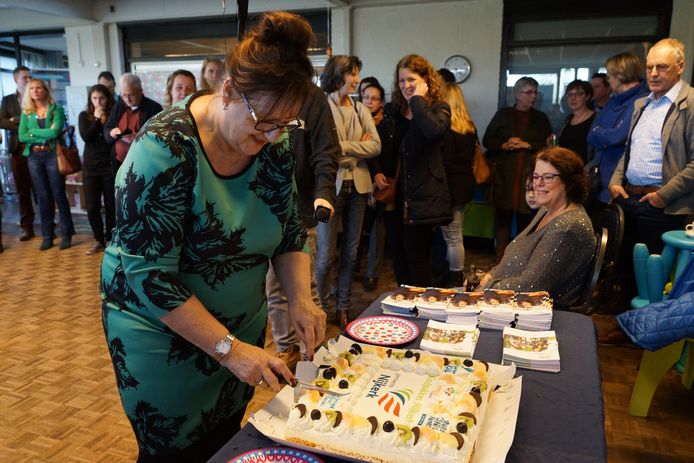 Wethouder Patricia van Loozen snijdt taart aan om het Kindpakket te vieren.
