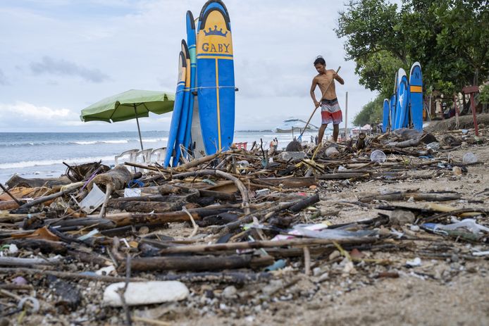 Een man kuist takken en plastic op het strand van Kuta op Bali op. Tijdens het regenseizoen komt er traditioneel heel wat troep terecht in de zee omdat het eiland geen gecentraliseerd afvalbeheersysteem heeft.