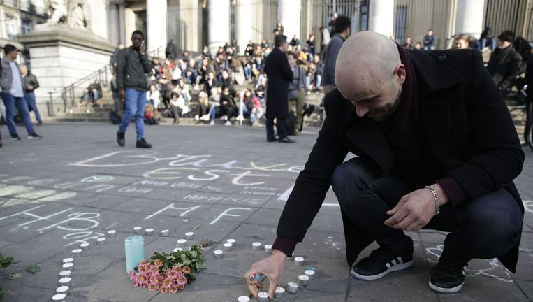 Een man steekt een kaarsje aan ter nagedachtenis aan de slachtoffers van de aanslagen in Brussel. Beeld afp