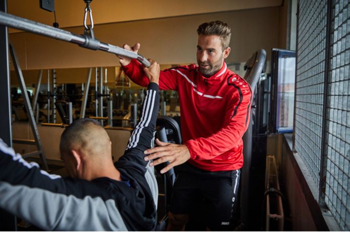 Sportinstructeur Daniel Wigman helpt een gedetineerde op de juiste manier een fitnessoefening te doen. De sportzaal heeft tralies.