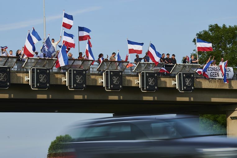 Op een viaduct boven de snelweg A4 staan sympatisanten van de boeren met omgekeerde Nederlandse vlaggen als blijk van hun ongenoegen tegen de stikstofmaatregelen. Beeld ANP / Nico Garstman