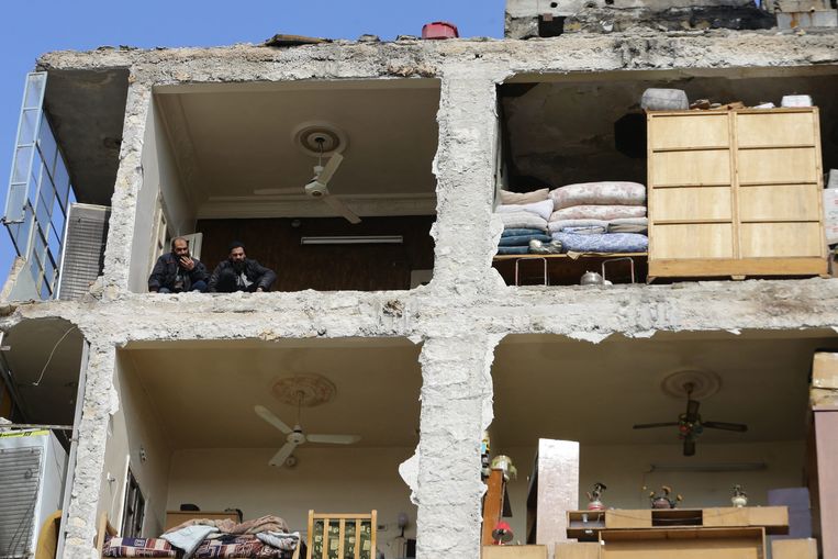 Twee mannen kijken de straat in vanuit een verwoest flatgebouw in de Syrische stad Aleppo.  Beeld AFP