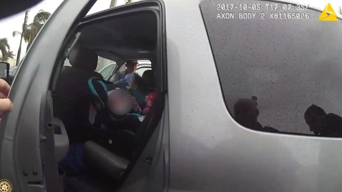 De politieagent troost één van de twee baby'tjes op de achterbank van de wagen, terwijl hun moeders worden verzorgd door hulpverleners.