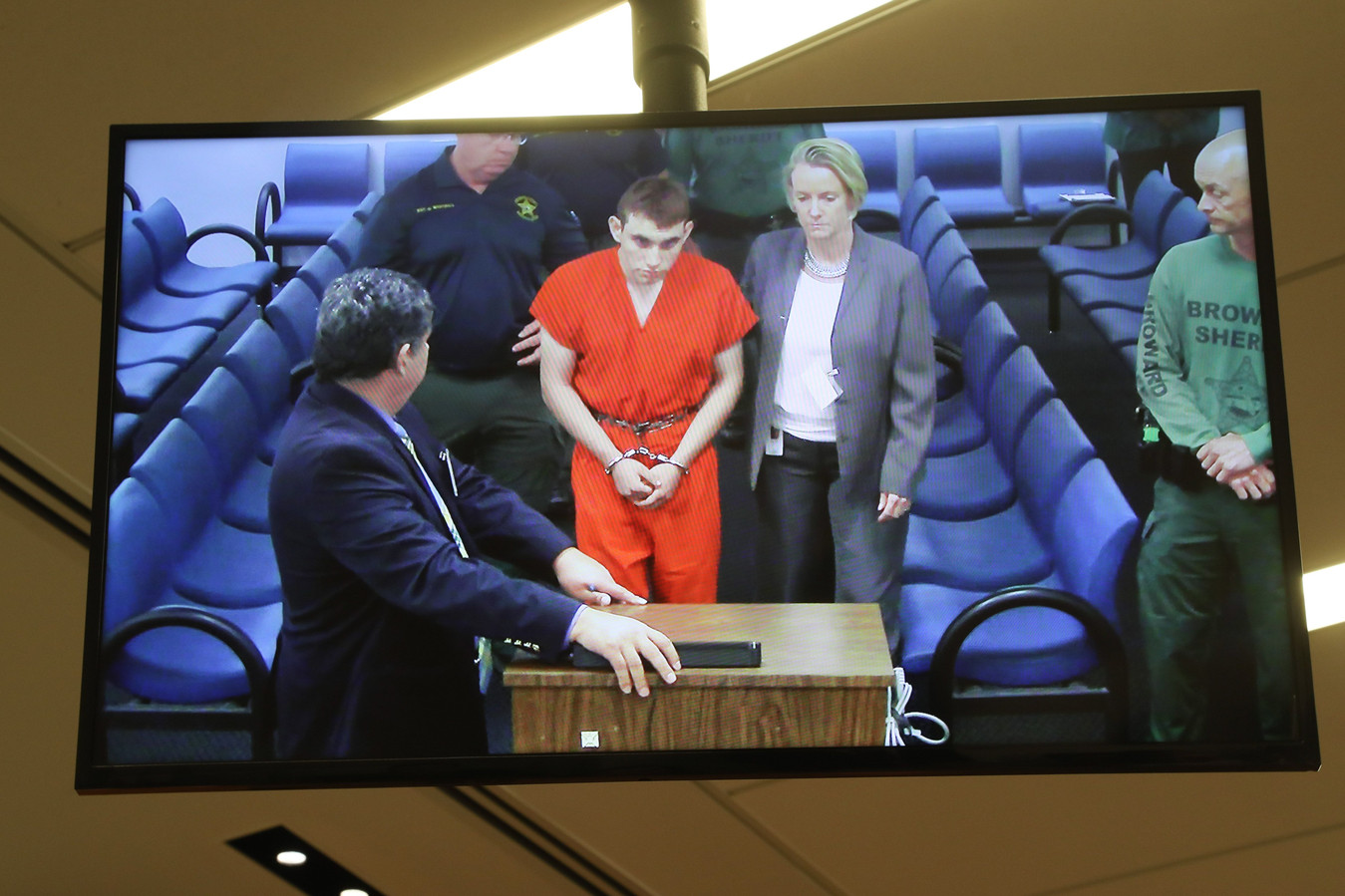 Op een televisiescherm is te zien hoe Nikolas Cruz wordt voorgeleid.