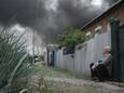 Een Oekraïense man zit bij zijn huis. Op de achtergrond is een rookpluim te zien door Russische bombardementen in Charkiv.