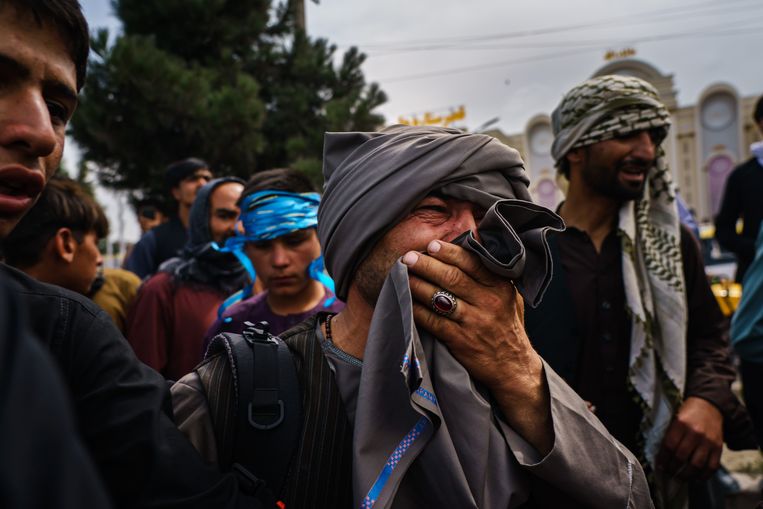 Een Afghaanse man kijkt vol afschuw naar talibanstrijders die met vuurwapens, zwepen en stokken de menigte te lijf gaan in de buurt van de internationale luchthaven in Kaboel.  Beeld Photo News