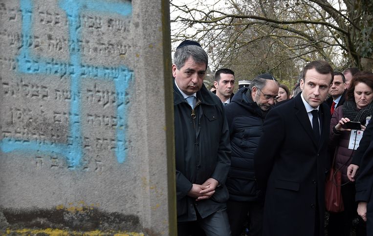 President Emmanuel Macron (r.) wandelde dinsdag tijdens een demonstratie tegen antisemtisme langs een met swastika’s beklad graf. Beeld REUTERS