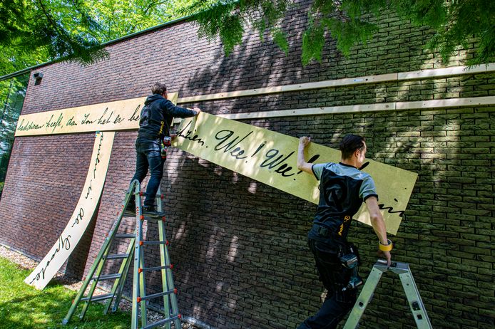 Werklui brengen op het Peerke Donders Paviljoen houten platen aan met een lang citaat uit een brief van de missionaris.