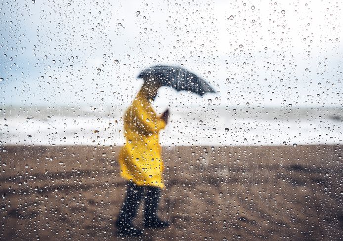 Man walking on the beach under heavy rain, viewed through windshield with raindrops